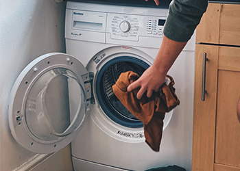 Mão colocando roupa suja na máquina de lavar